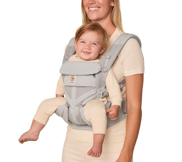 A woman gently holds a baby in a front-facing baby carrier, smiling as they share a moment together.