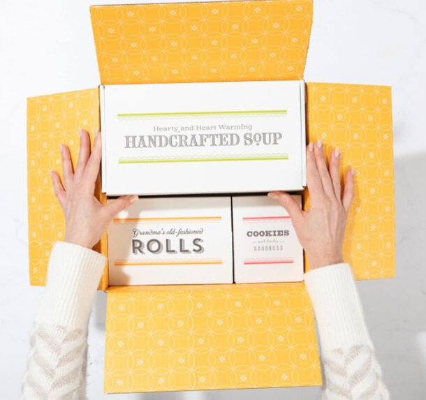 A woman holds a box of handmade soup, showcasing its artisanal packaging and inviting design.
