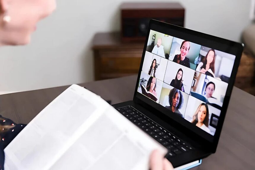 A woman gazes at a laptop screen displaying a group of people engaged in a virtual meeting.