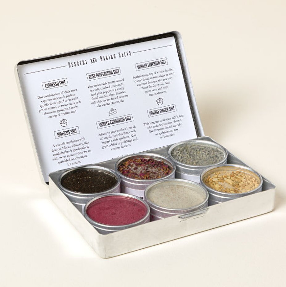 A tin box containing six assorted body care products, including lotions and creams, arranged neatly inside.