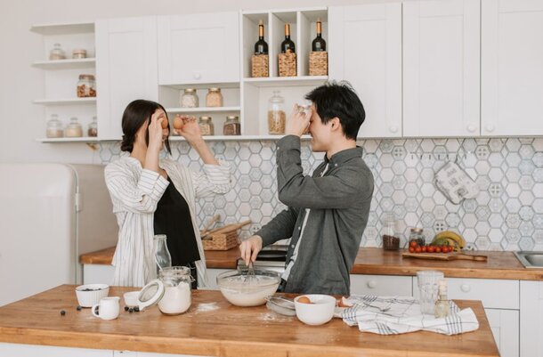 A couple joyfully cooking together in a bright kitchen, surrounded by fresh ingredients and kitchen utensils.