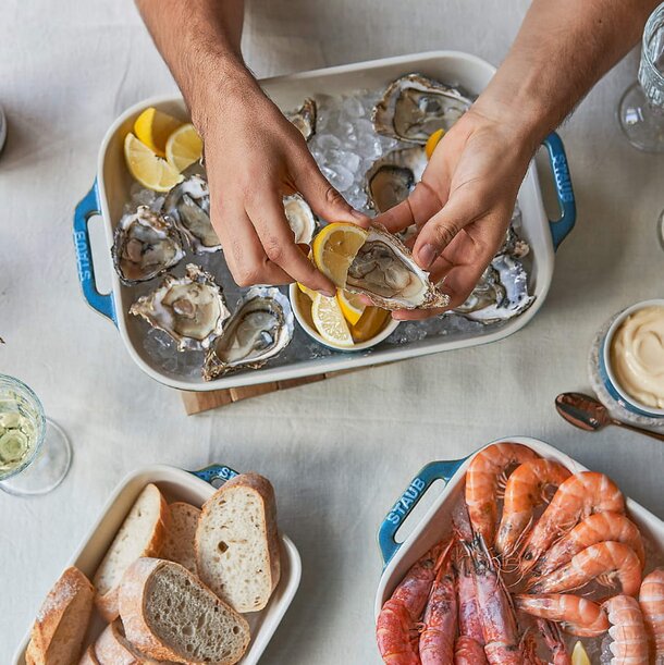 A person holds a tray filled with an assortment of seafood and slices of bread, ready to be served.