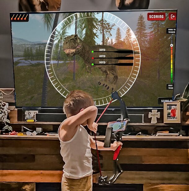 A young boy aims a bow and arrow while watching a related scene on a television screen.