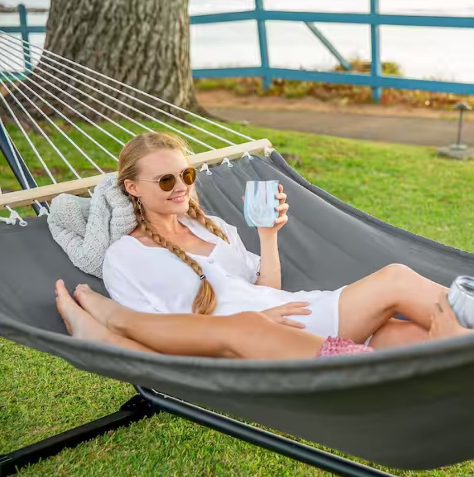 Two women relax in a hammock, each holding a cup of coffee, enjoying a peaceful moment together outdoors.