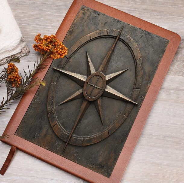 A compass notebook rests beside a flower and a folded towel on a textured surface.