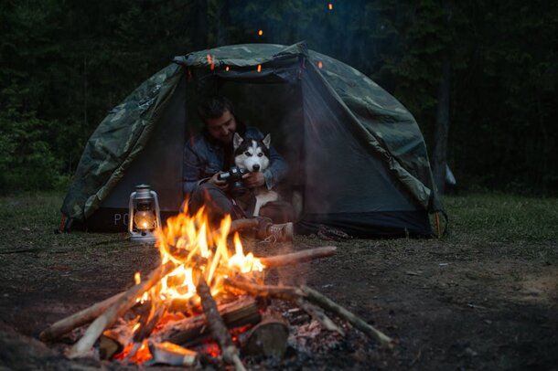 A man and his dog sit together by a campfire, enjoying the warmth and glow of the flames in a serene outdoor setting.