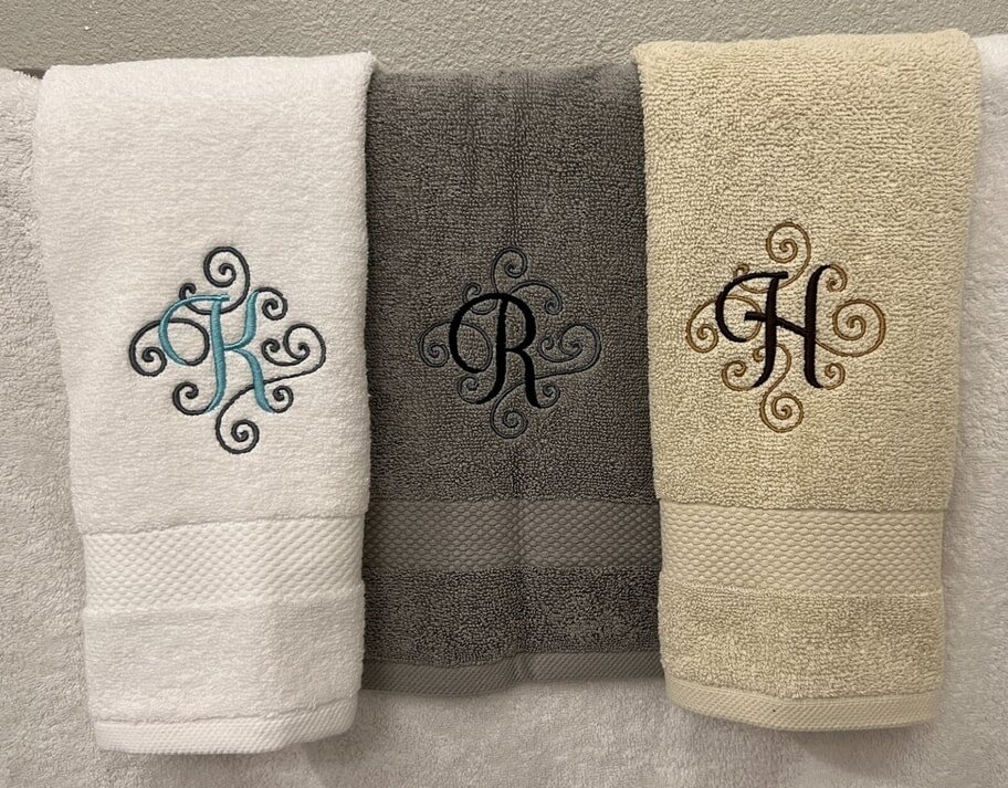Three neatly arranged towels featuring elegant monogrammed initials on each one.