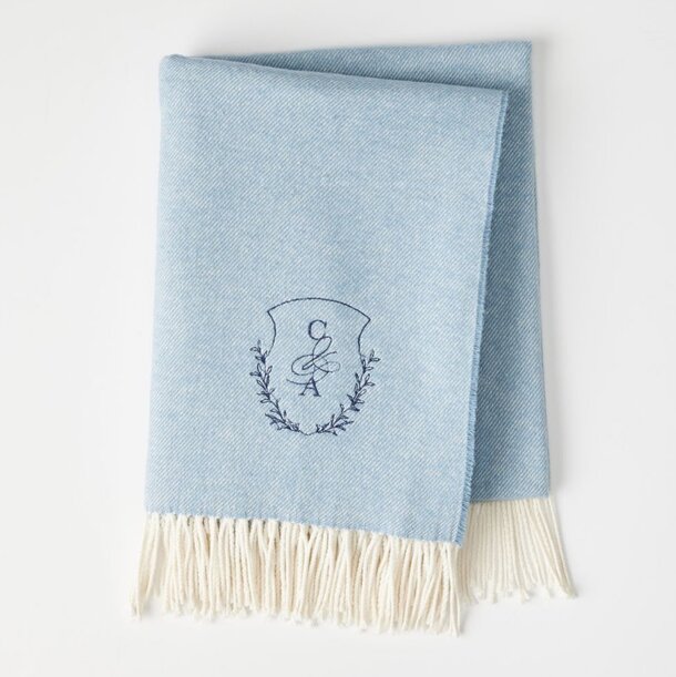 A blue blanket featuring a white embroidered crest in the center.