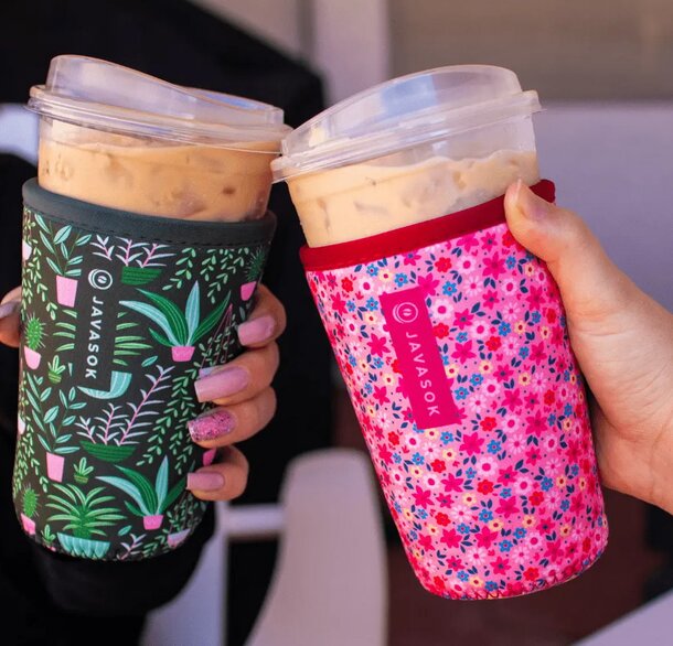 Two people joyfully hold up coffee cups topped with scoops of ice cream, smiling at the camera.  