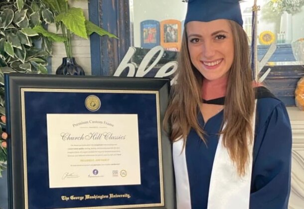 A woman in a graduation gown proudly holds a framed certificate, celebrating her academic achievement.