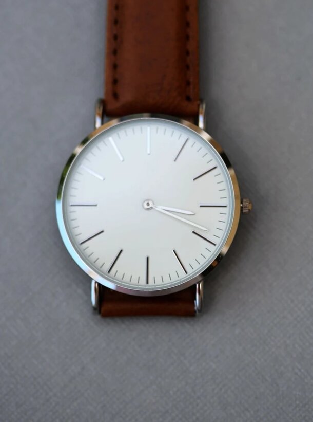 A white watch with a brown leather strap displayed on a gray background.