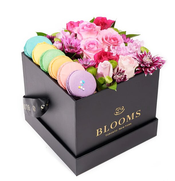 A decorative box filled with colorful flowers and an assortment of macarons arranged neatly.