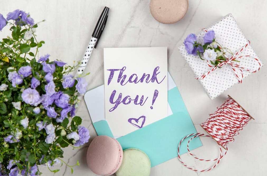 Thank you card adorned with flowers and a gift, set against a sleek marble background.