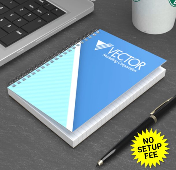 A4 spiral notebook beside a pen and a coffee mug on a wooden table, suggesting a workspace setup. 