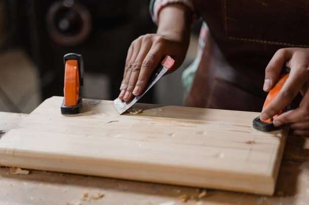 A person skillfully cutting wood with a knife on a wooden cutting board.