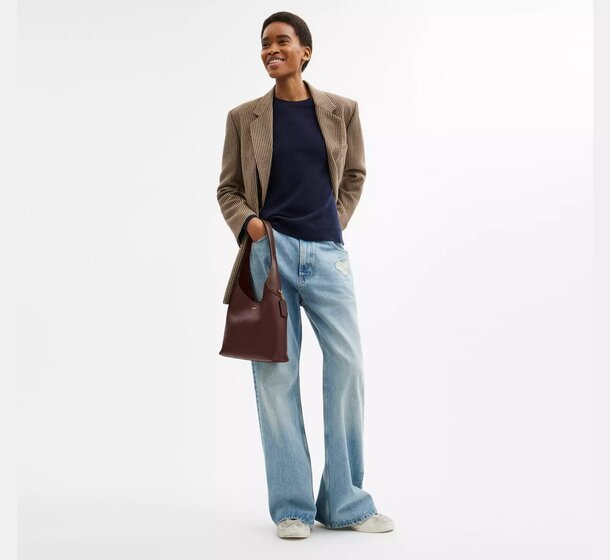 A woman in a stylish blazer and jeans poses confidently for the camera, showcasing a modern and professional look.