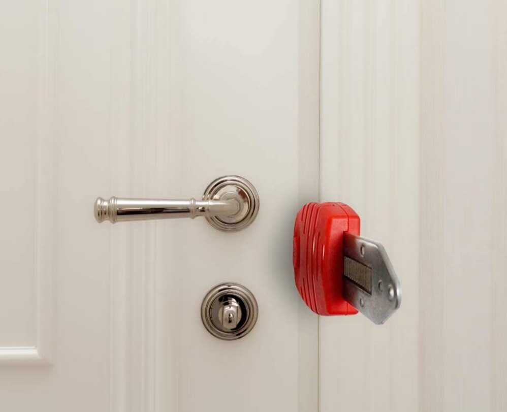 Close-up of a white door with a silver handle and lock, featuring a red security device installed over the door lock mechanism, conveying protection and safety.