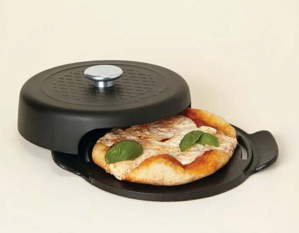 A pizza cooks in a pan on a kitchen counter, with melted cheese and toppings visible.