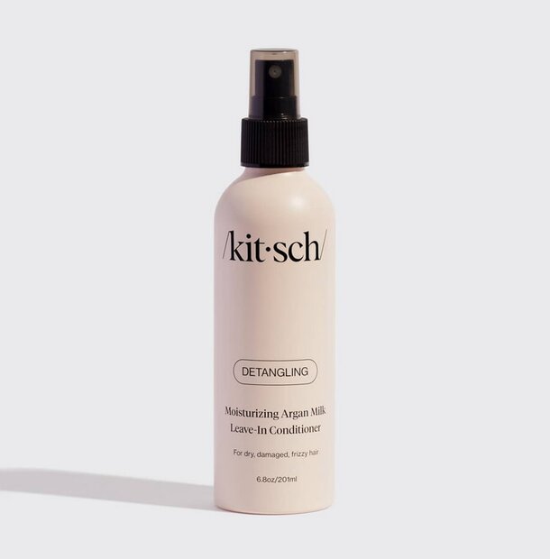 Kitsch hydration mist bottle with a colorful design, surrounded by tropical leaves and flowers on a light background.  