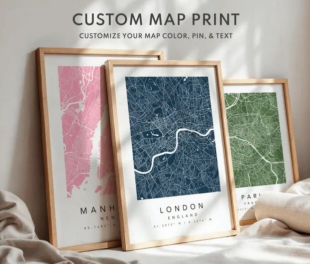 Framed custom map prints displayed, featuring cities with different colored backgrounds: pink for Manhattan, blue for London, green for Paris.