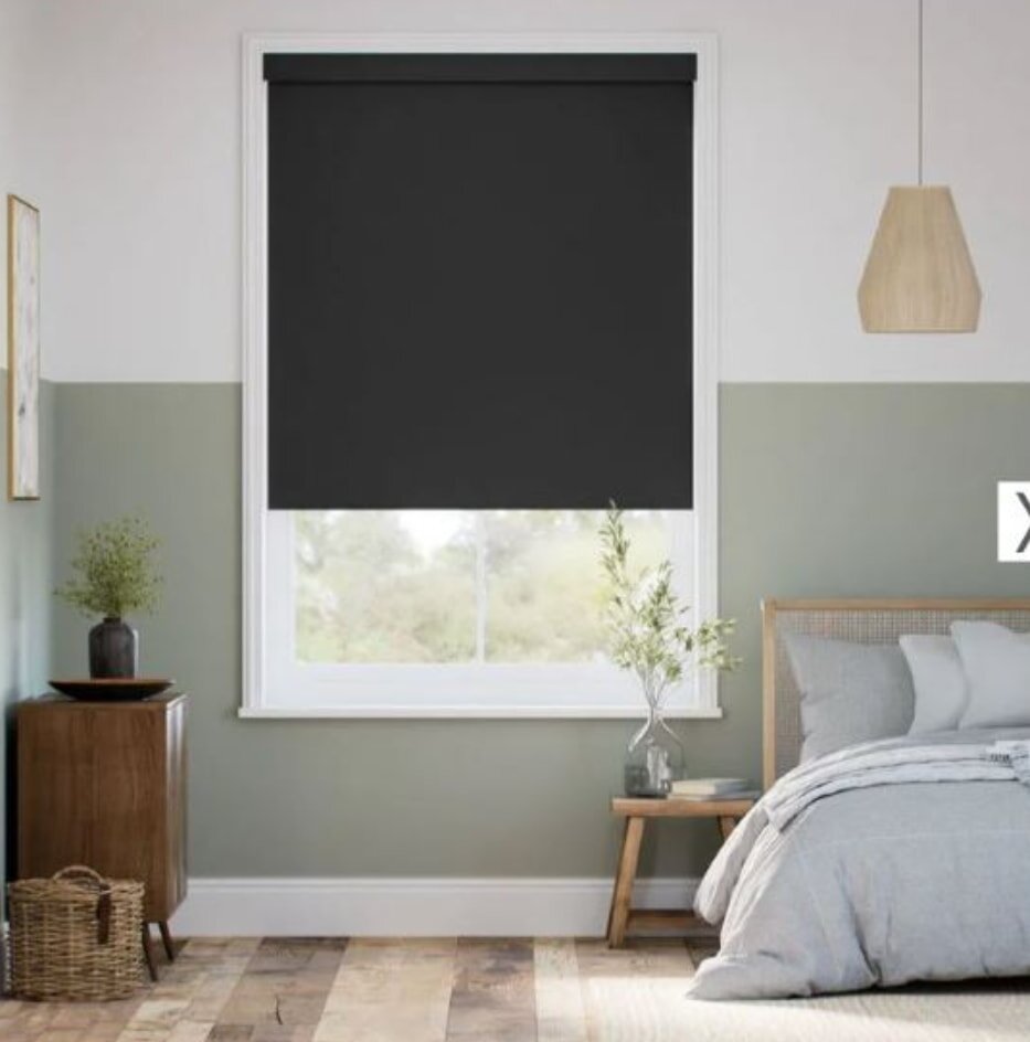 A neatly arranged bedroom with a black roller blind covering the window, creating a darkened atmosphere.
