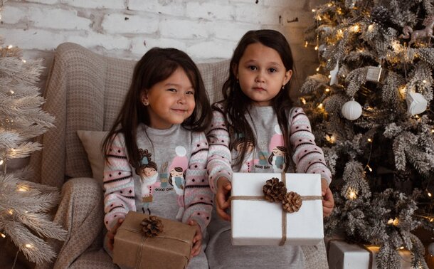 Two little girls joyfully hold presents in front of a beautifully decorated Christmas tree.