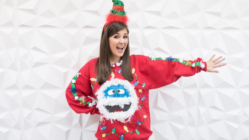 A woman in an ugly sweater and a Santa hat smiles cheerfully, embodying festive holiday spirit.