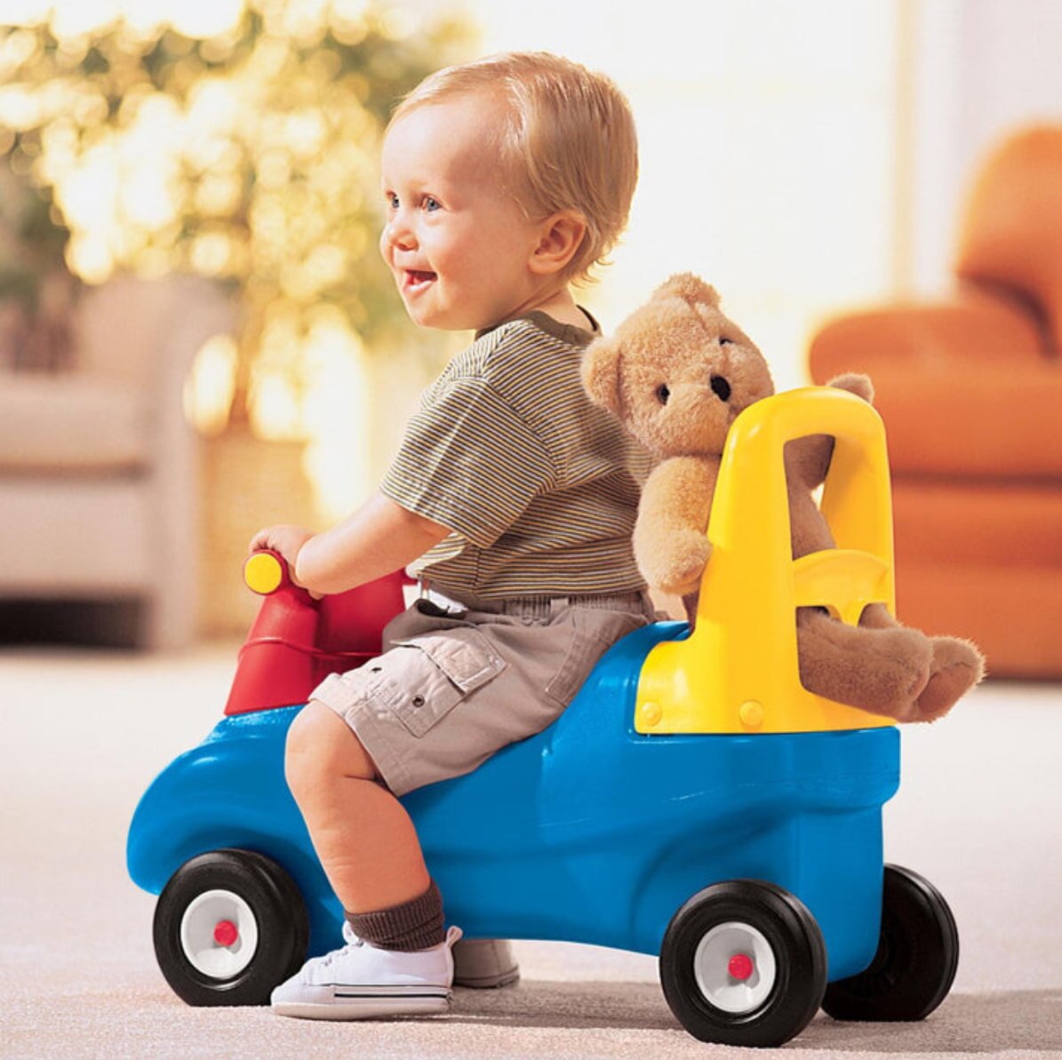 A small child happily riding a bright red toy car on a smooth surface, enjoying their playtime outdoors.