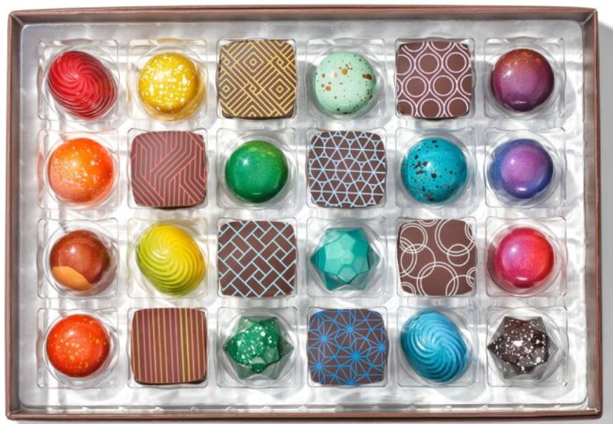 A box of 24 colorful, assorted chocolates arranged in four rows. Each piece has unique designs and patterns, creating an artistic and luxurious feel.