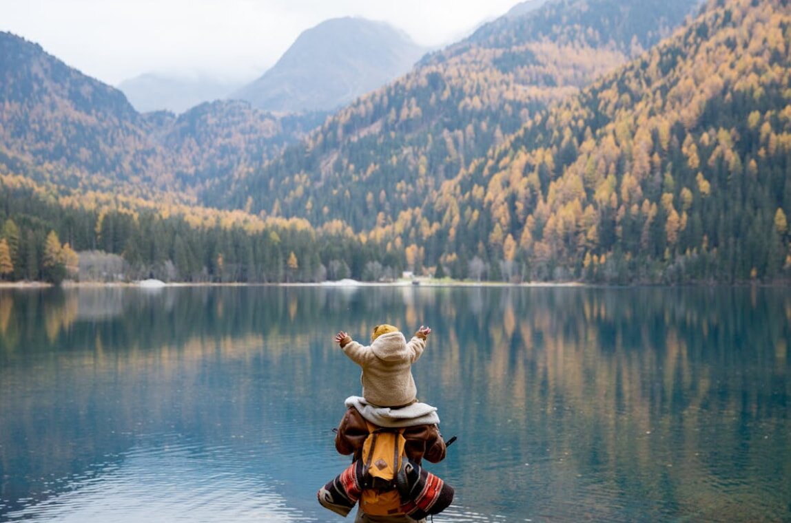 A young child perched on a rock beside a tranquil lake, enjoying the peaceful scenery and natural surroundings.