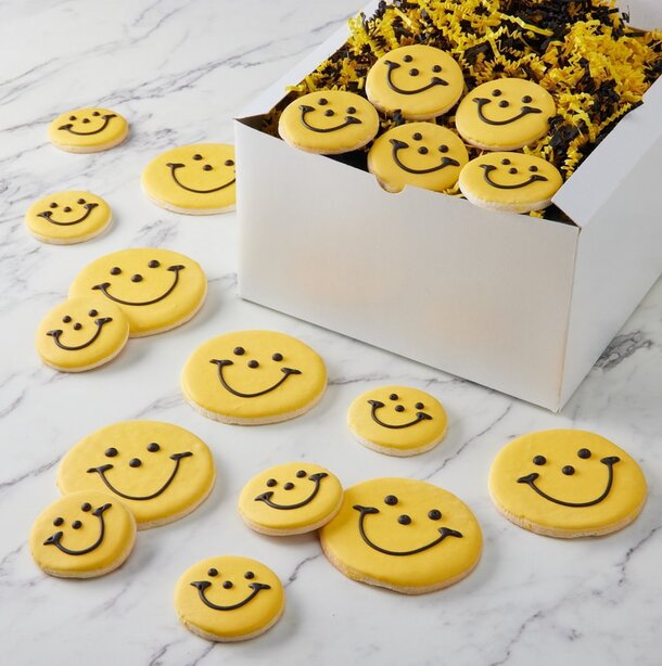 A box filled with smiley face cookies, each decorated with cheerful expressions and vibrant colors.