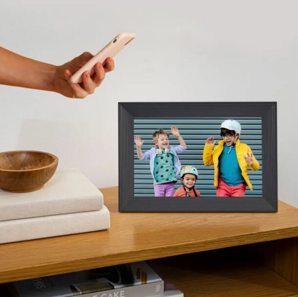A person holds a cell phone beside a picture frame, showcasing a blend of technology and personal memories.