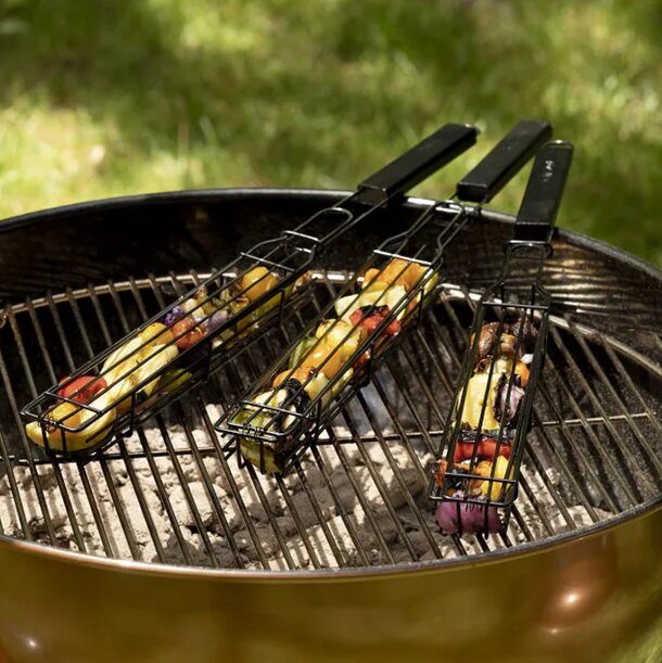 Three skewers of food are placed on a grill beside a metal grill basket, ready for cooking.