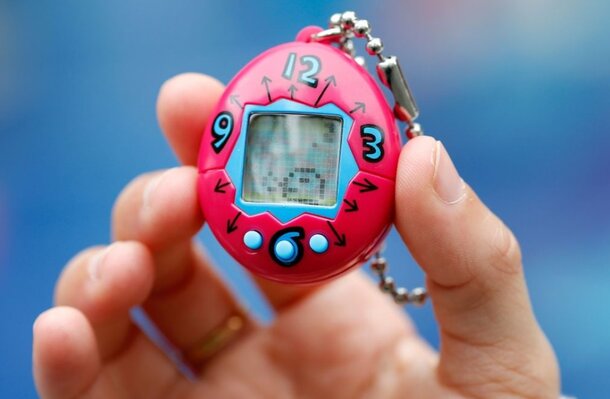 A person holds a pink toy featuring a small clock, showcasing a playful design and vibrant color.