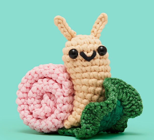 A crocheted snail with a green leaf on its shell, showcasing intricate stitching and vibrant colors.