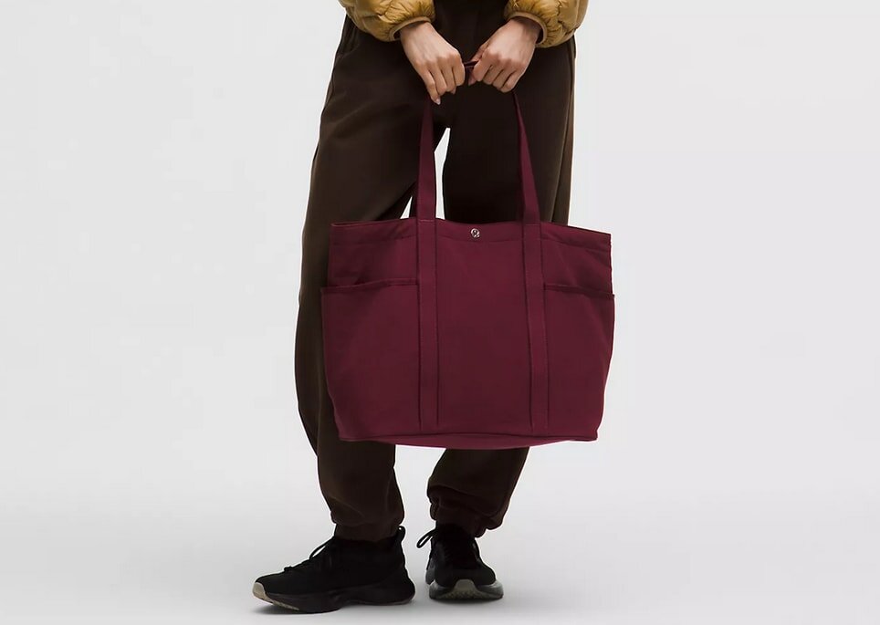 A woman is holding a large tote bag, showcasing its size and design.