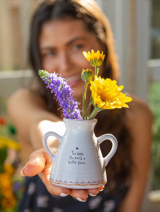 A woman holding a vase filled with colorful flowers, smiling gently as she admires her arrangement.