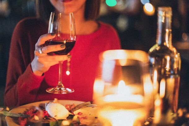 A woman holding a glass of wine, seated at a table in a restaurant, enjoying her dining experience.