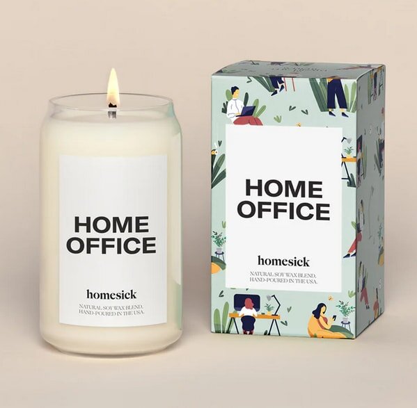 A lit "Home Office" candle by Homesick beside its colorful box, creating a cozy workspace ambiance.