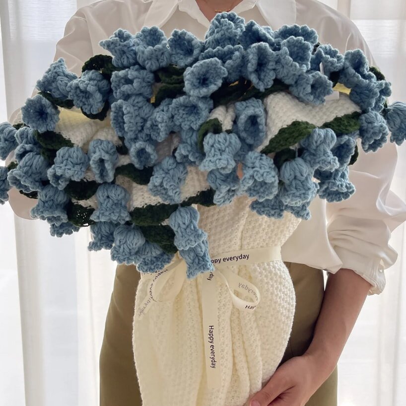 A woman holds a crocheted bouquet featuring vibrant blue flowers, showcasing her crafting skills and creativity.