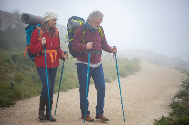 Two hikers with backpacks walking along a foggy trail, surrounded by mist and trees, creating a serene atmosphere.
