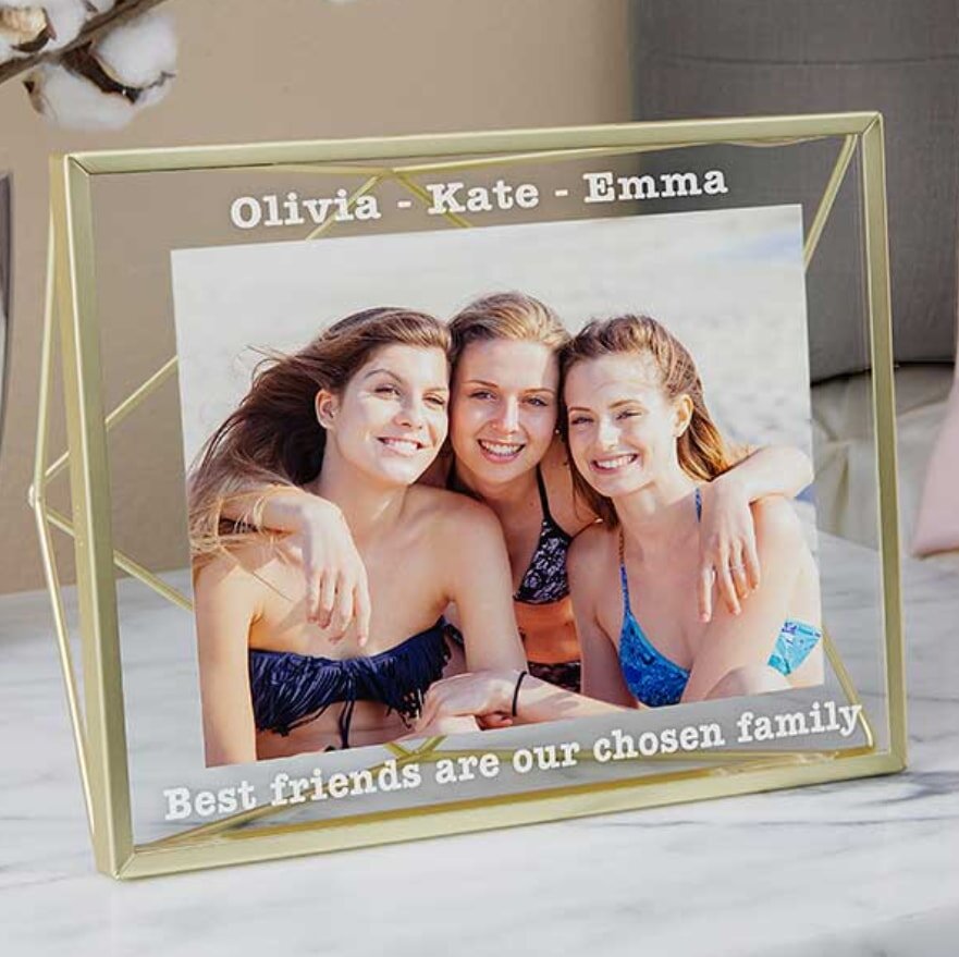 A framed photo shows three smiling women in swimsuits on a beach, arms around each other. The frame reads, "Olivia - Kate - Emma" and "Best friends are our chosen family."