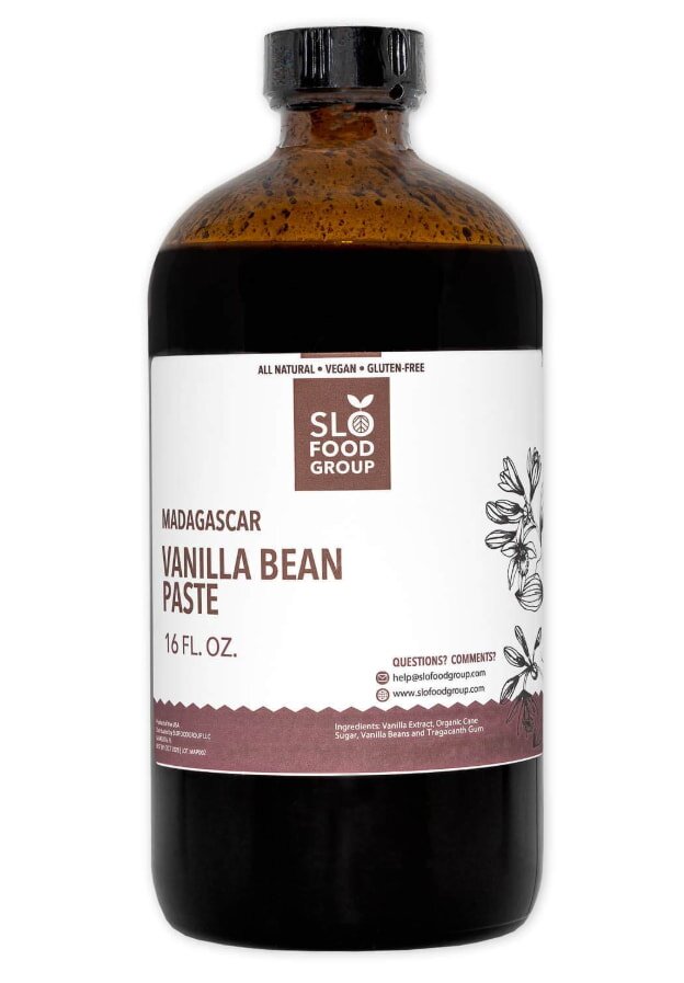 A bottle of vanilla bean extract surrounded by sugar, highlighting its use in baking and flavoring desserts.