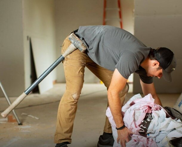 A man is using a hammer to work on a house, focused on a construction task.