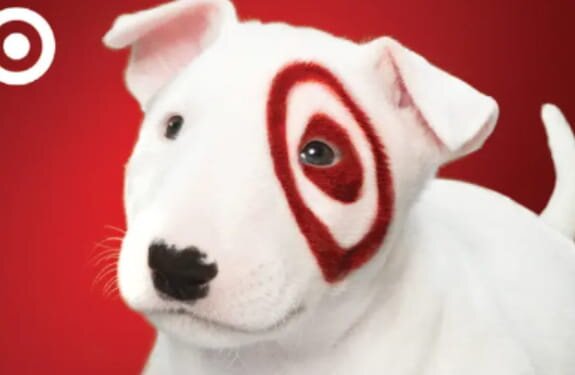 A white dog with a red target logo prominently displayed on its face, looking directly at the camera.