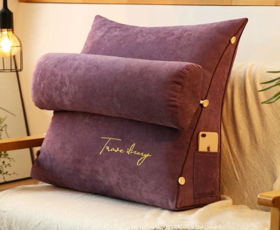 Plush purple backrest pillow with a detachable bolster and "Travel Library" embroidered. It has button details and a phone pocket, creating a cozy vibe.