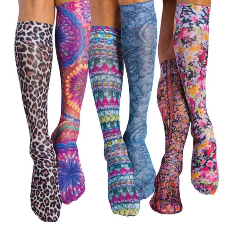Three women's legs wearing vibrant, colorful socks in various patterns, standing side by side on a light surface.