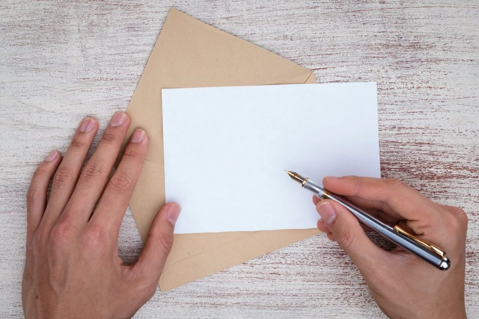 A hand holds a pen, writing on an envelope, capturing a moment of correspondence.