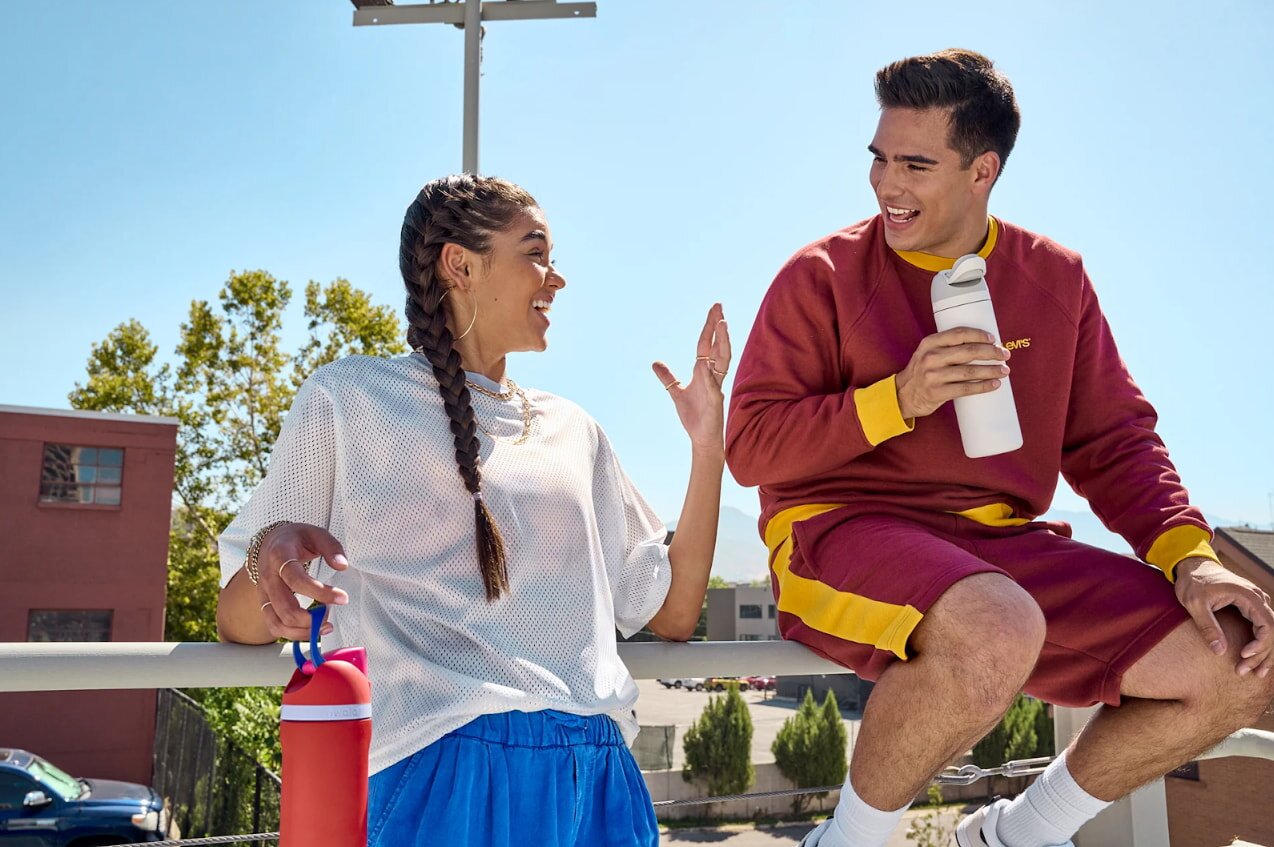 A man and woman sit on a bench, sharing a moment together with a water bottle placed between them.