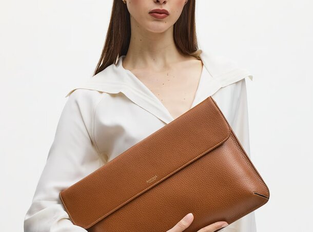 A woman holds a stylish brown leather clutch in her hand, showcasing its elegant design.